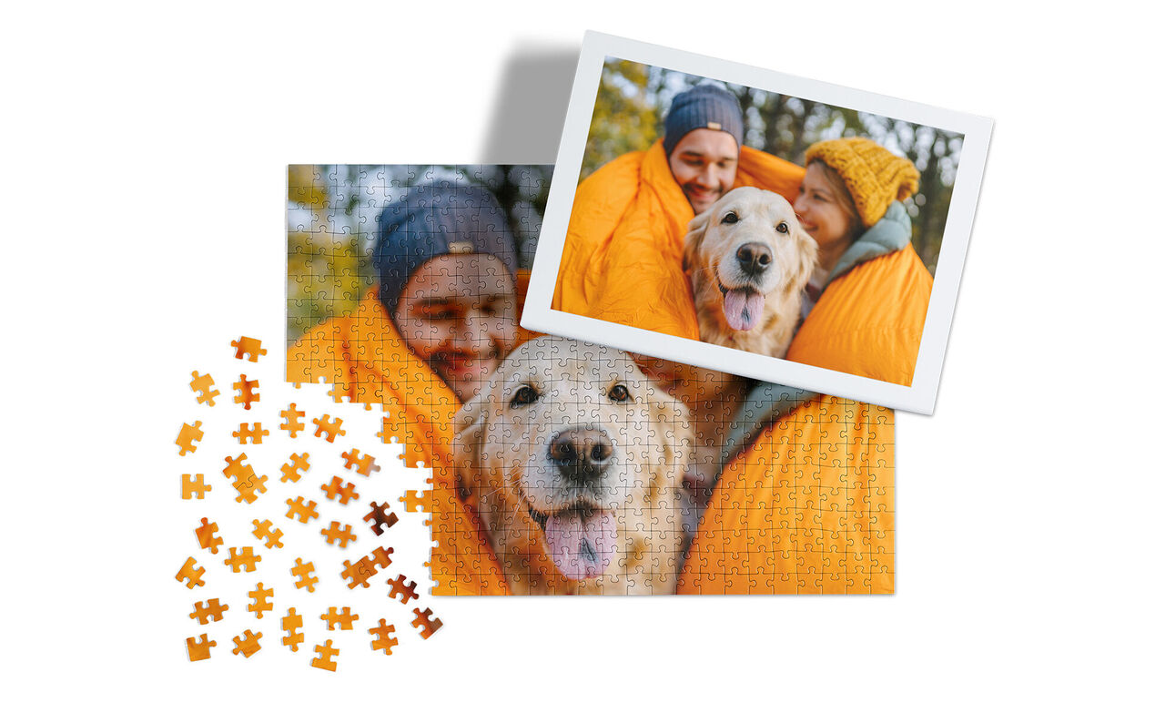 Zwei glückliche Hunde in einer orangefarbenen Decke, umgeben von Puzzlestücken